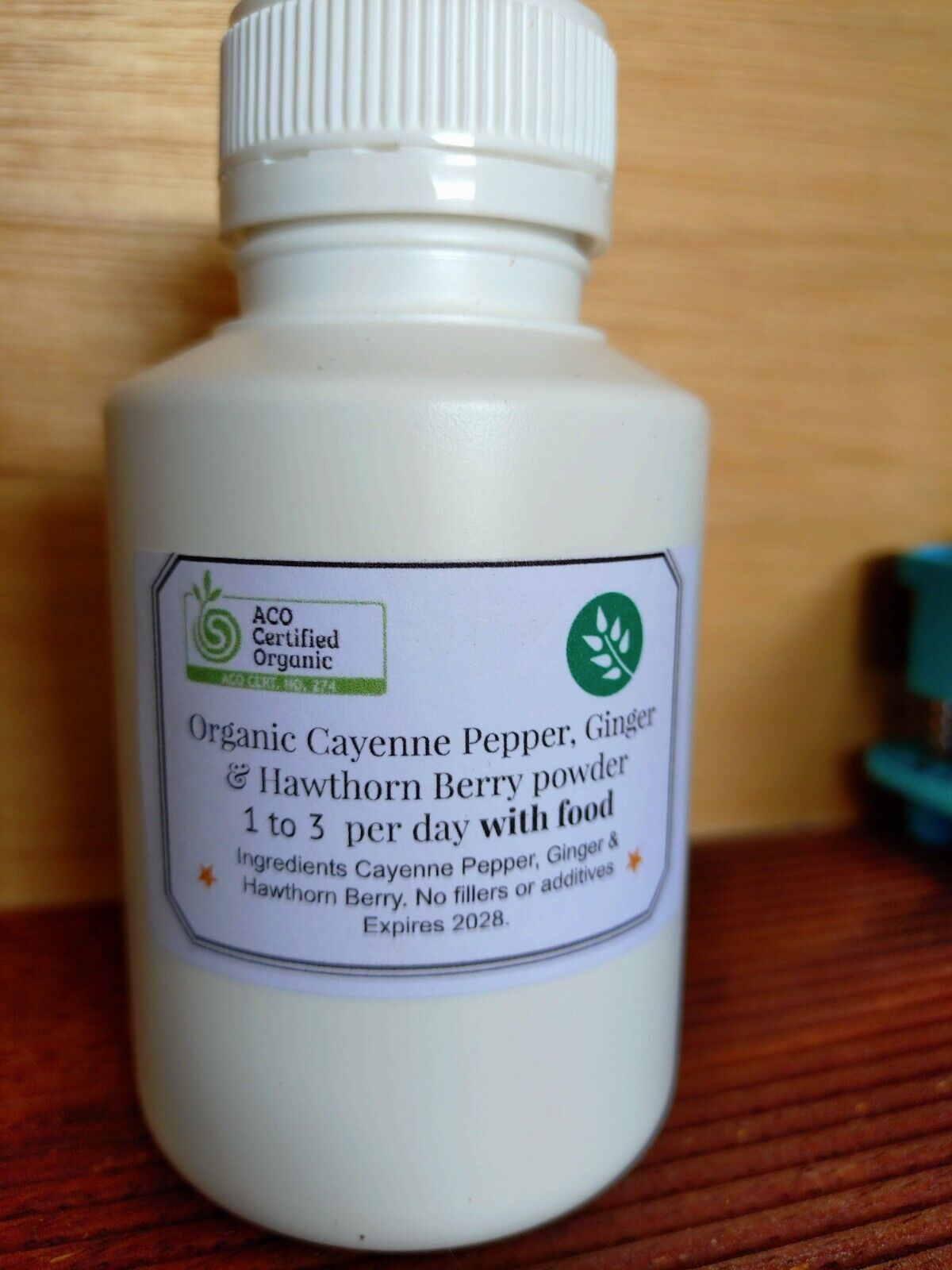 A bottle of organic cayenne, ginger, and hawthorn berry capsules with a white label on a wooden surface.