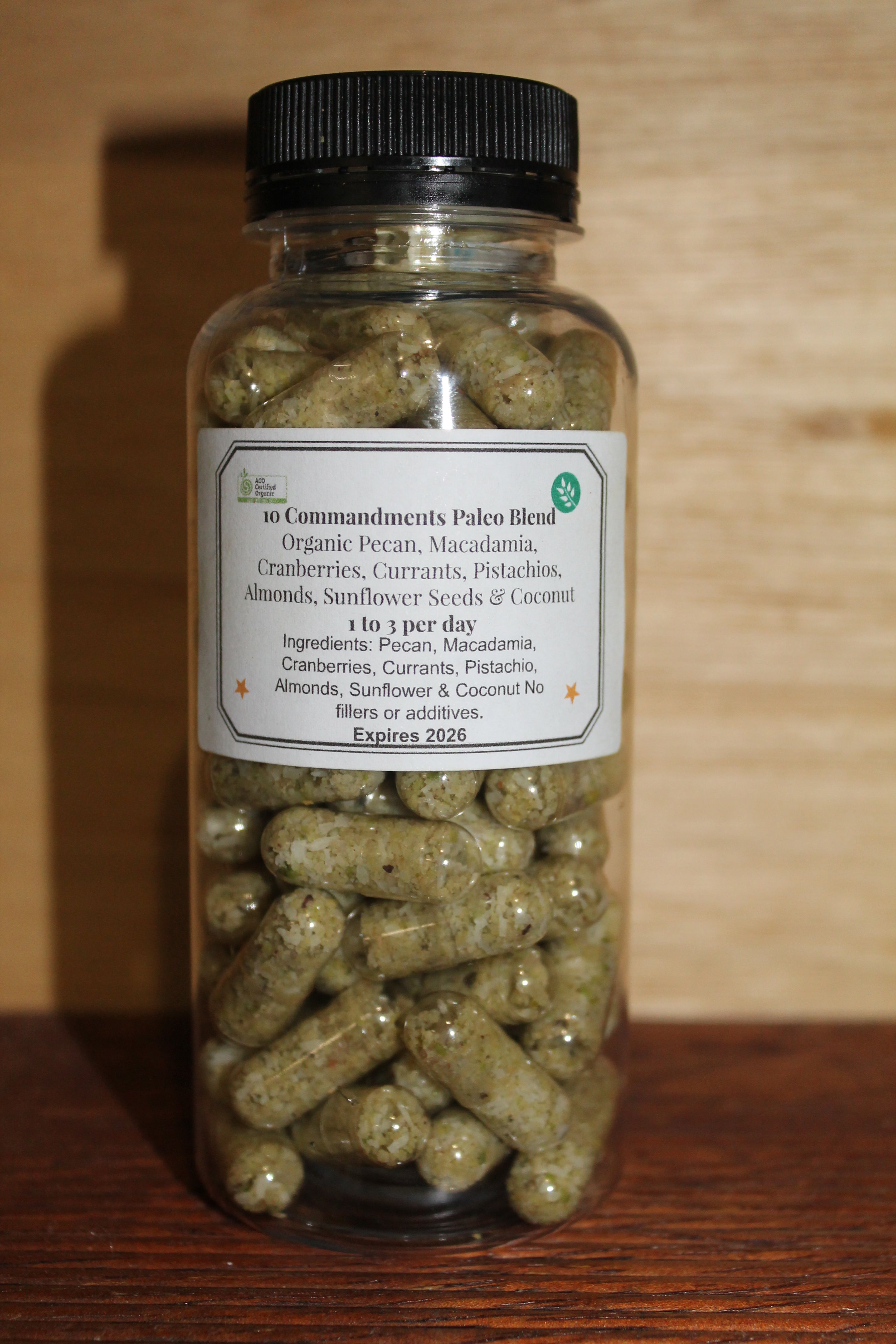 A clear plastic bottle with a black lid containing green capsules labeled as '10 Commandments Paleo Blend - Organic Superfood Capsules'.